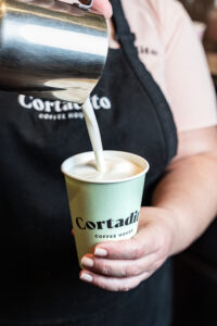 Latte at Cortadito (alt text: Barista pouring textured milk into a Cortadito Coffee House cup, showcasing the preparation of authentic specialty coffee in Miami